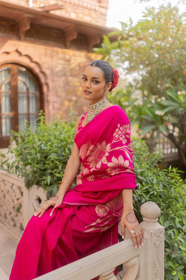 Woman in a bright pink saree with white patterns sitting outdoors.
